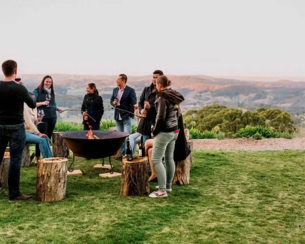 Staff retreat ideas for nonprofits: A group enjoys a bonfire and drinks outdoors, surrounded by rolling hills.