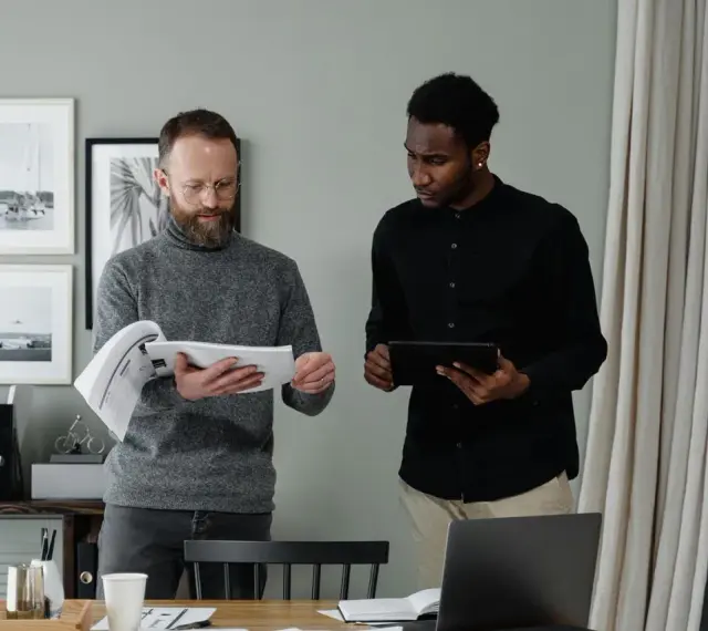 Two men review documents and a tablet, discussing the details of in-kind donation accounting.